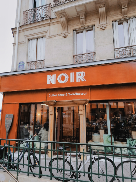 Coffee shop in Paris with bikes parked along the fence out front. White letters on an orange background: "NOIR."