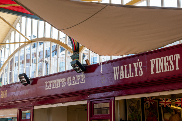 Inside Market Hall in Stockport, UK. Red background, off-white painted text in various typefaces. "LYNN'S CAFE" "WALLY'S FINEST"