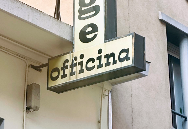 Estro on Torino signage. Black letters on a white background on a store sign perpendicular to the building read: "officina." Photo by Giuseppe Salerno.
