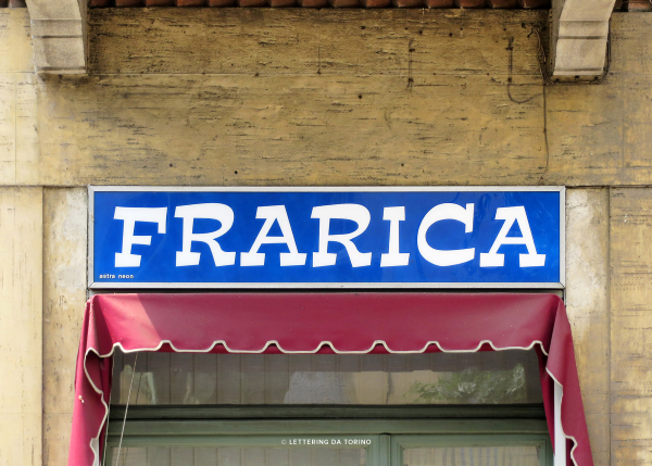 Estro signage in Torino. White all-caps letters on a bright blue background read: "FRARICA" above a short red curtain store awning. Photo from Lettering da Torino.