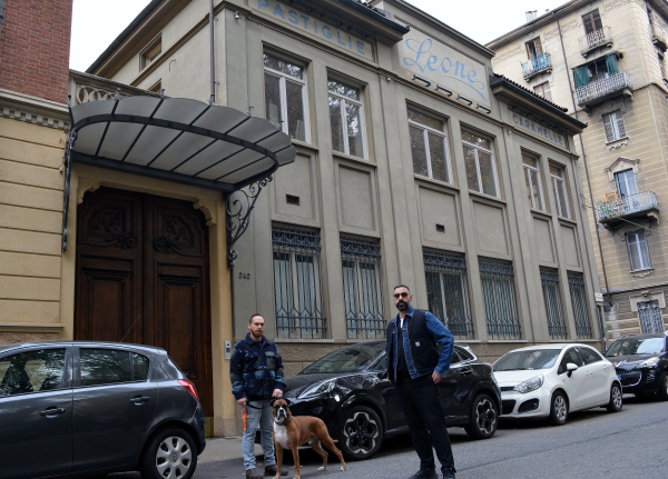 Resistenza Type with Paco (left) and Giuseppe (right). Photo by Daniel Rocco. Two men with a dog stand on a car lined street outside the Leone building.