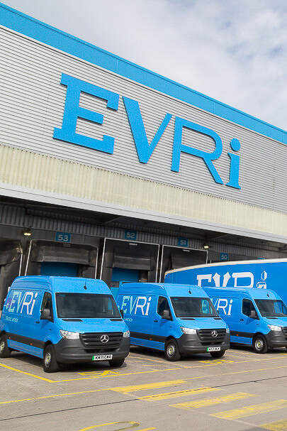 Blue Evri delivery vans parked at the loading bays of a warehouse with a large Evri logo on the front.