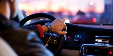 A man is shown driving a car as if the viewer is in the back seat.