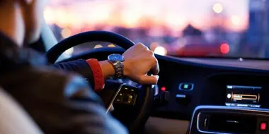 Man driving a car A man is shown driving a car as if the viewer is in the back seat.