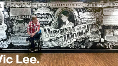 Photo of artist Vic Lee sitting in front of a typographic mural celebrating the life of Virginia Woolf