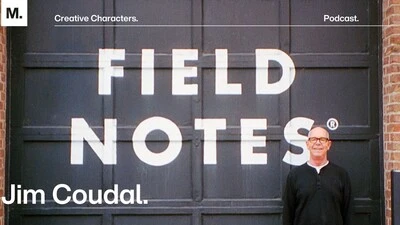 Field Notes founder Jim Coudal standing in front of a black and white mural that reads "Field Notes."
