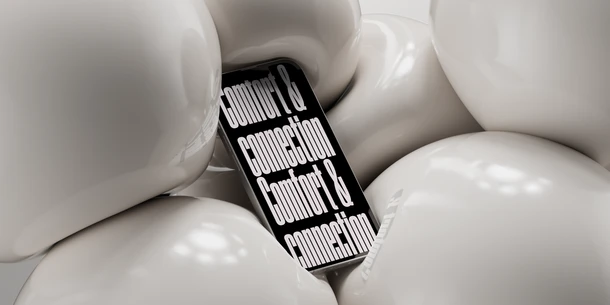A phone pictured squished between several white balls. Black background with white text: "comfort & connection Comfort & connection"
