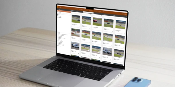 A laptop computer screen displaying the Portrait DAM. The computer sits on a desk with a smartphone face down next to it.