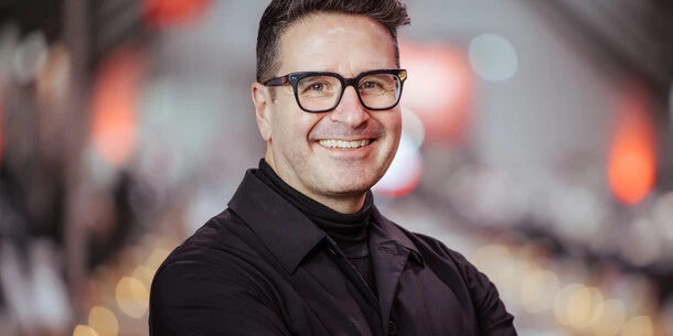 Headshot for Charles Nix, wearing a black shirt pictured in front of a dynamic background with lots of bokeh.