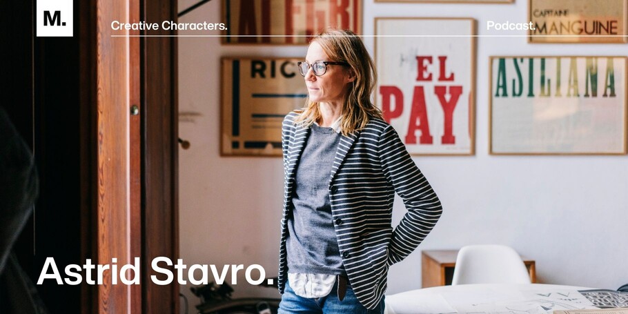 Astrid Stavro standing in a well lit room with framed typographic posters on the wall behind her.