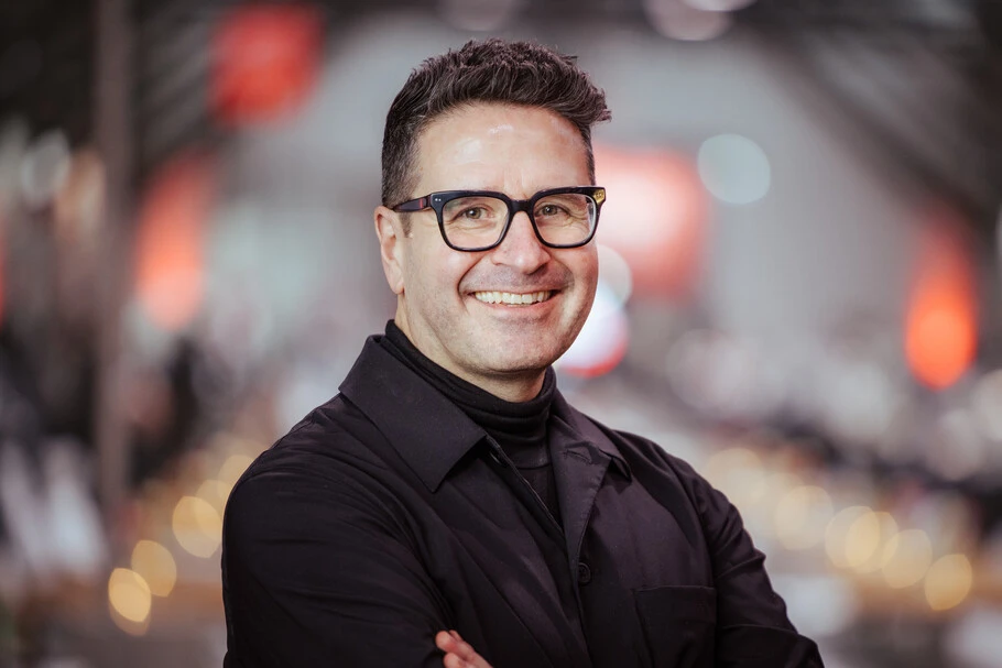 Headshot for Charles Nix, wearing a black shirt pictured in front of a dynamic background with lots of bokeh.