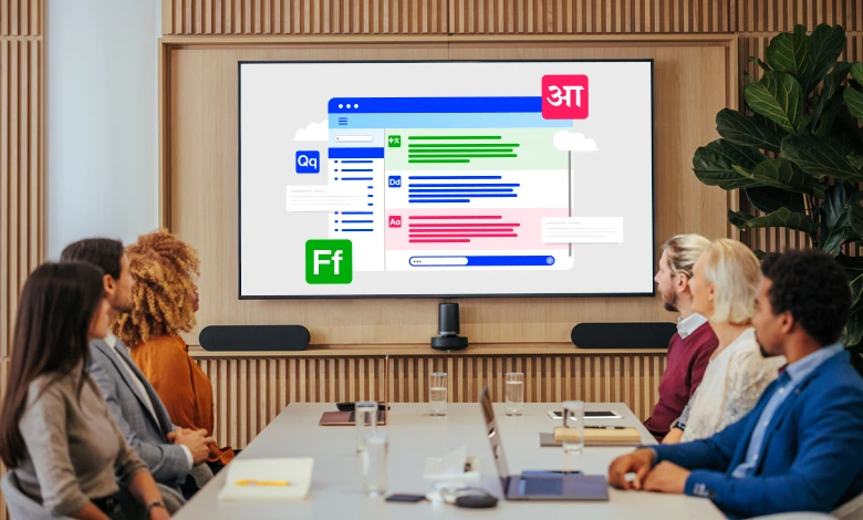 People sit at a meeting room table watching a presentation on a larger screen. The screen contains layered boxes with glyphs and lines suggestive of additional text in a variety of colors (blue, green, red).